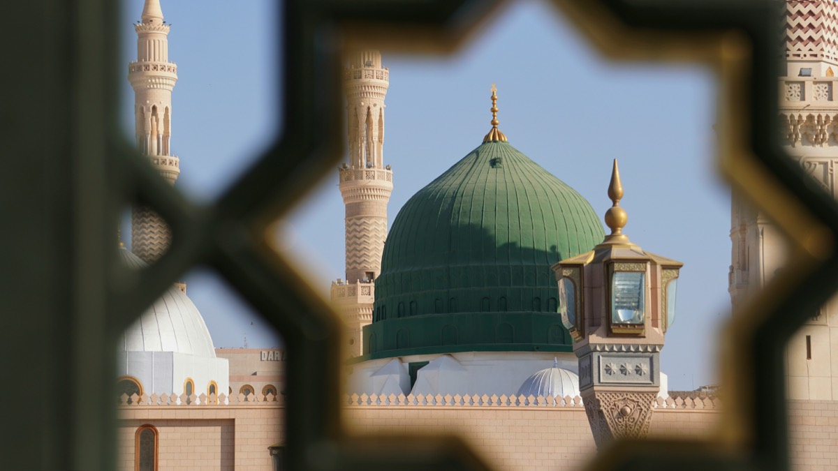 The green dome of the Prophet's Mosque in Madinah, seen through a patterned screen