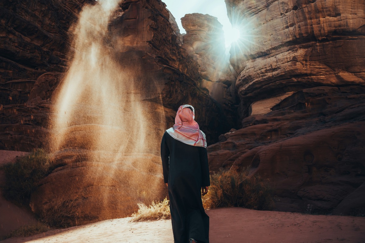 A traveller in a keffiyeh standing in a sunlit sandstone canyon in Saudi Arabia